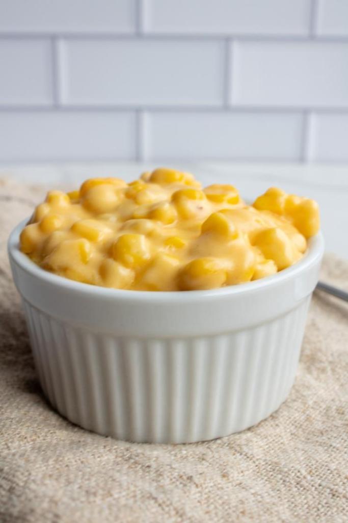 Cheesy creamed corn is presented in a small ramekin with a subway tile backsplash behind it.