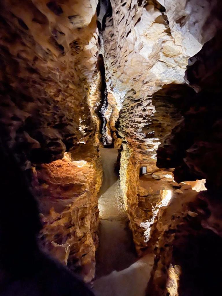A narrow passageway is shown in a dark, lit up cave.