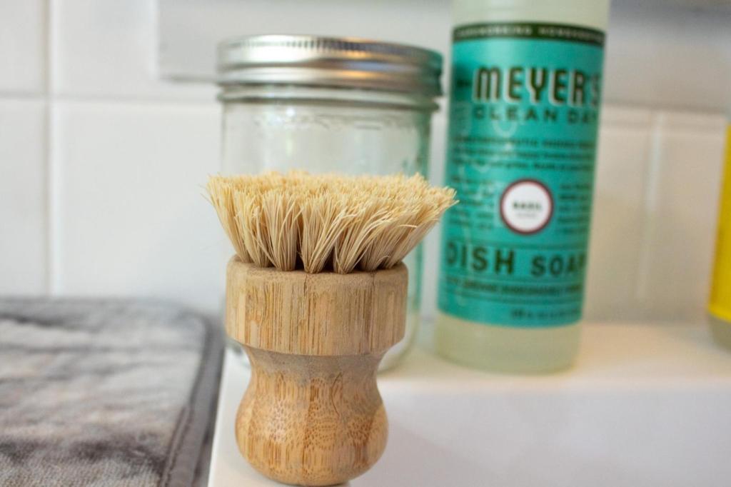 A bristled bamboo dish scrubber is shown in front of soap and baking soda.