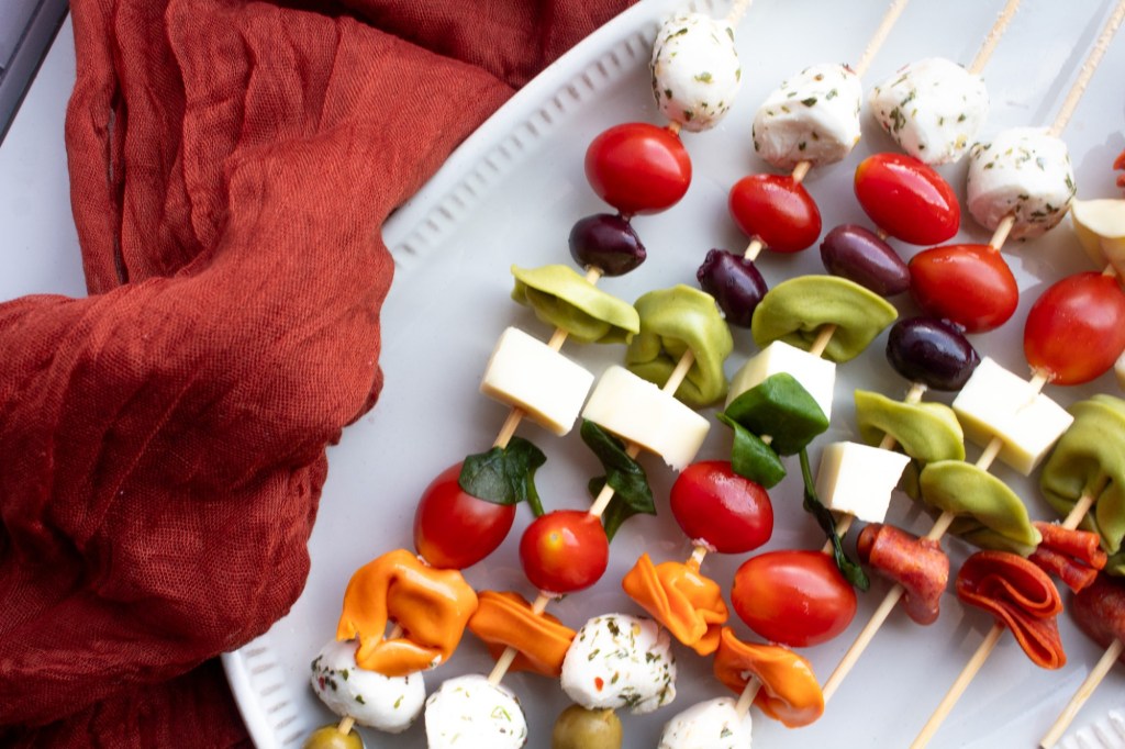 Italian antipasti skewers are laid on a plate over a red tablecloth.