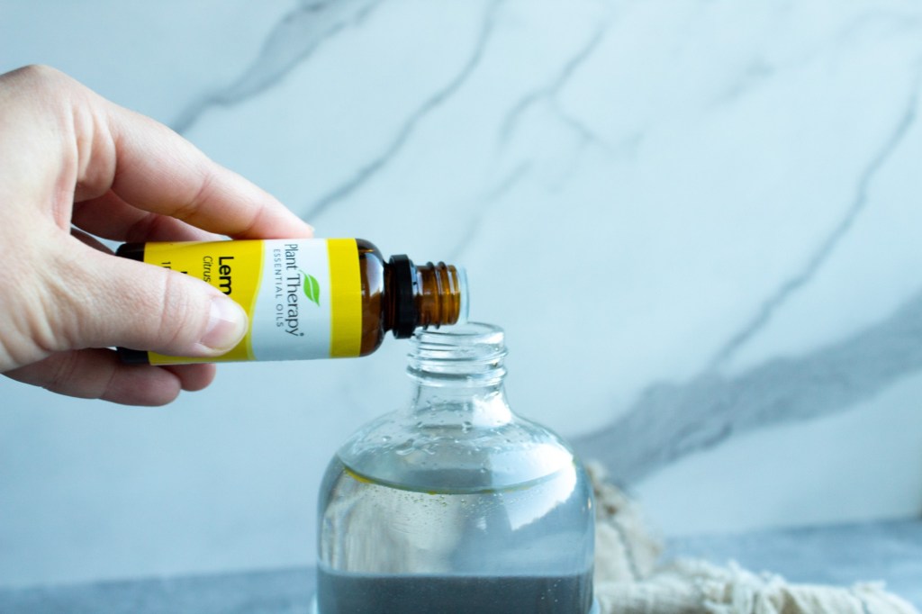 A woman pours lemon oil into a bottle of water and vinegar.