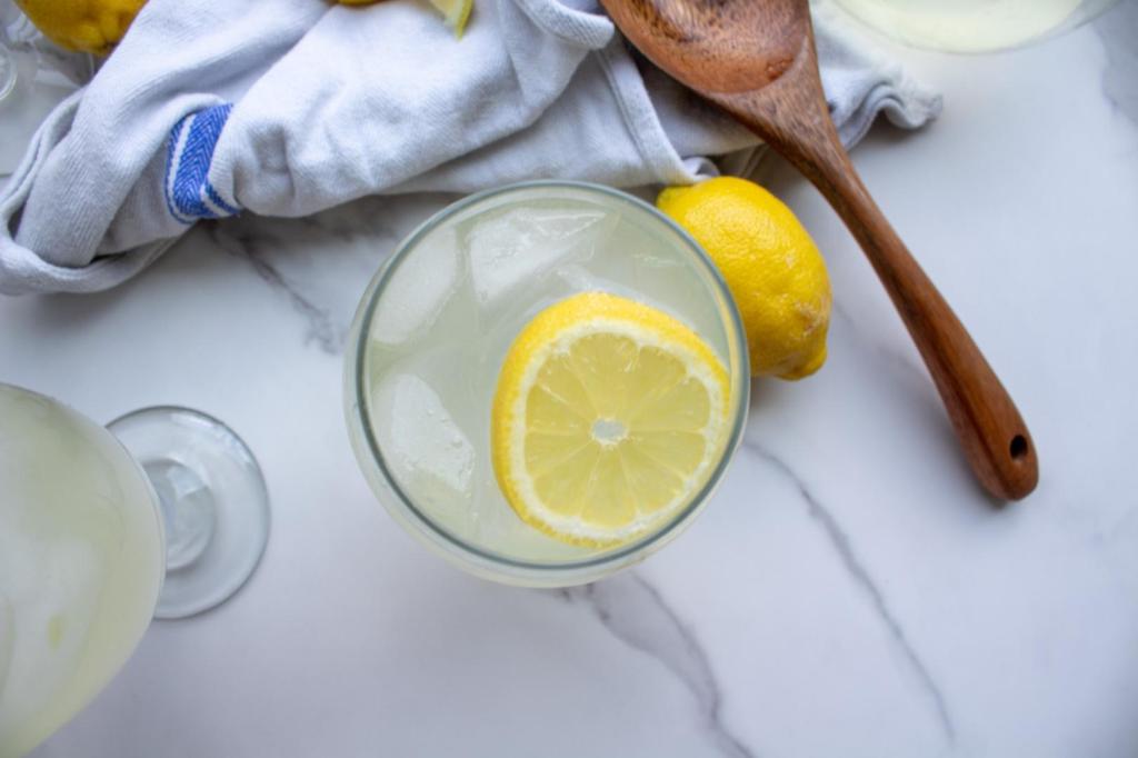 Homemade lemonade with simple syrup is shown in a glass with a lemon slice inside it.