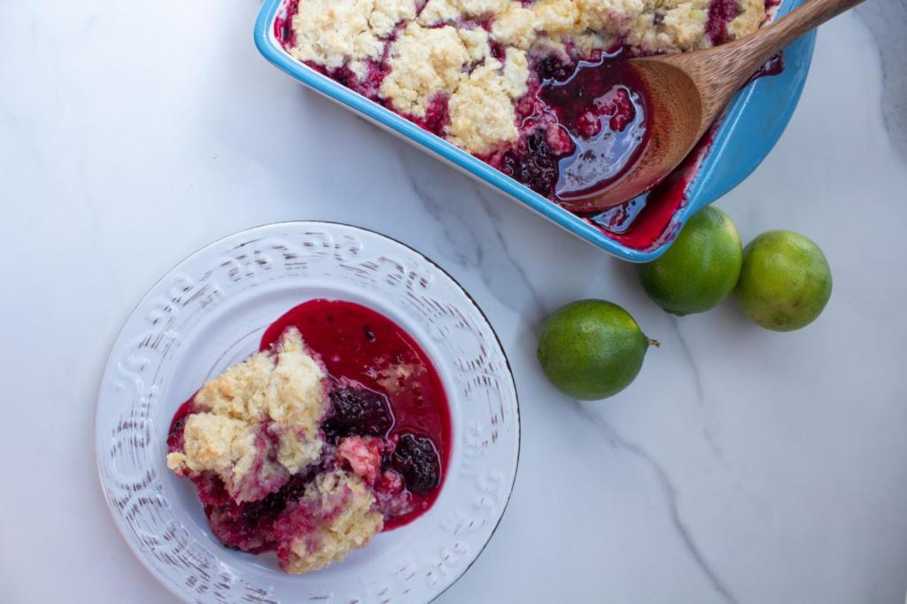 Easy blackberry cobbler is served alongside limes with the large dish of cobbler behind it.