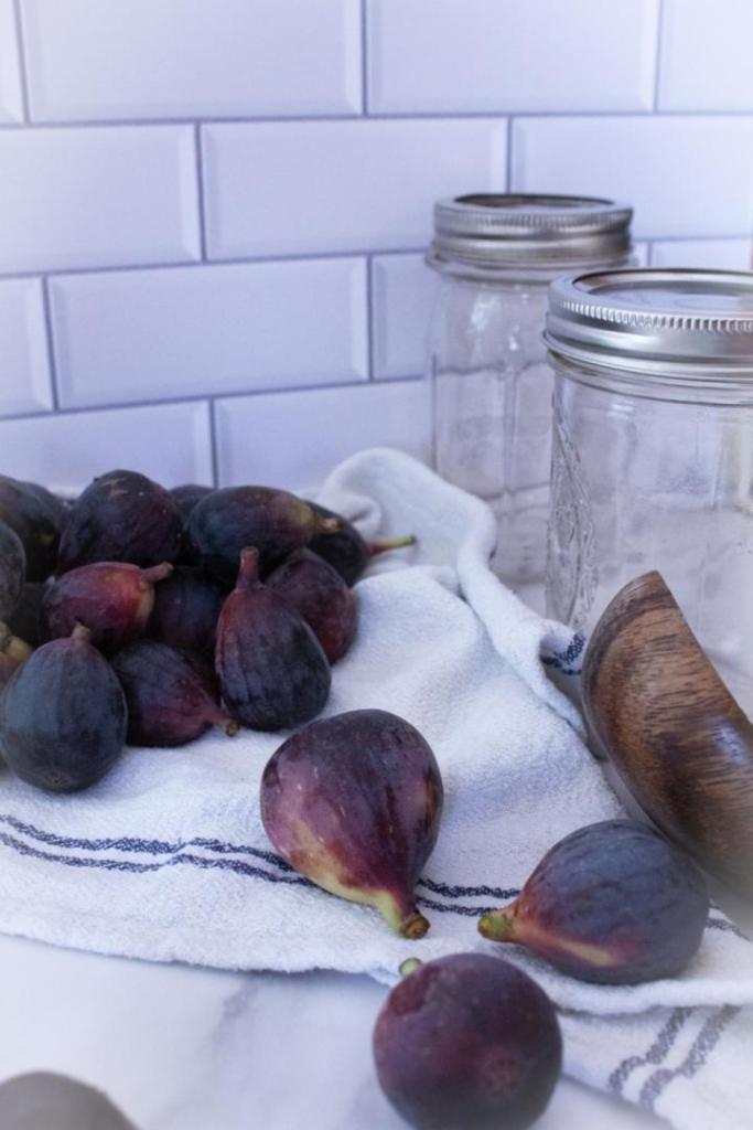 Figs lay on a linen towel near a wooden ladle and glass jars.
