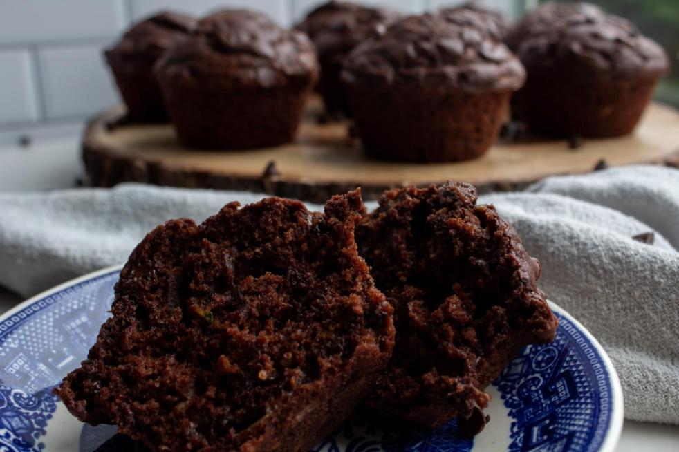 Double chocolate zucchini muffins are organized on a platter with a saucer of a split muffin in front.