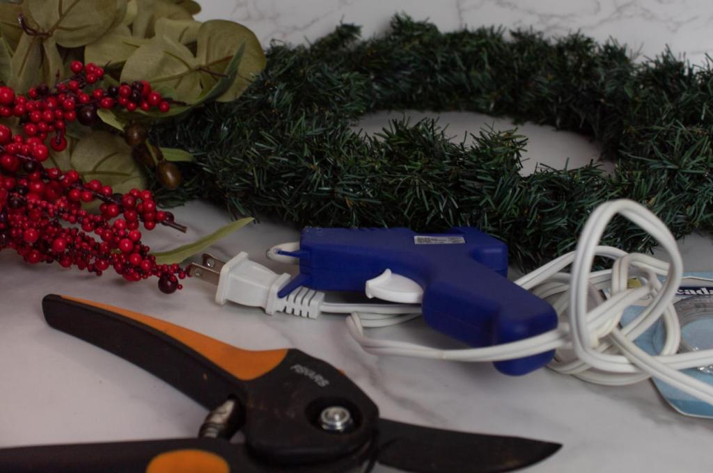 Supplies for a DIY eucalyptus Christmas wreath are scattered on a table.