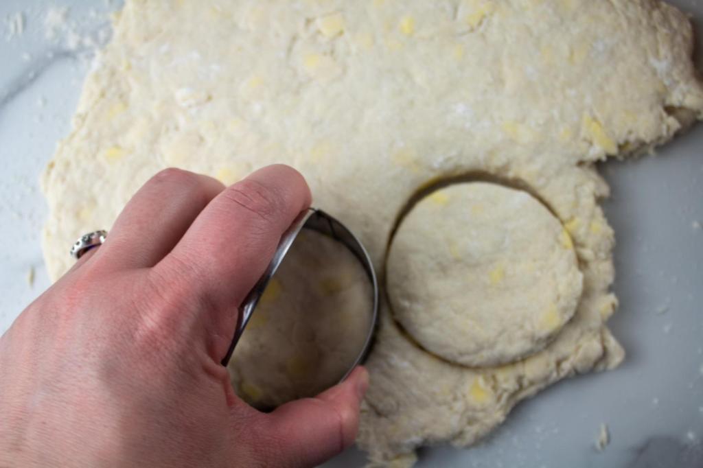 A woman uses a biscuit cutter to make disks of dough.