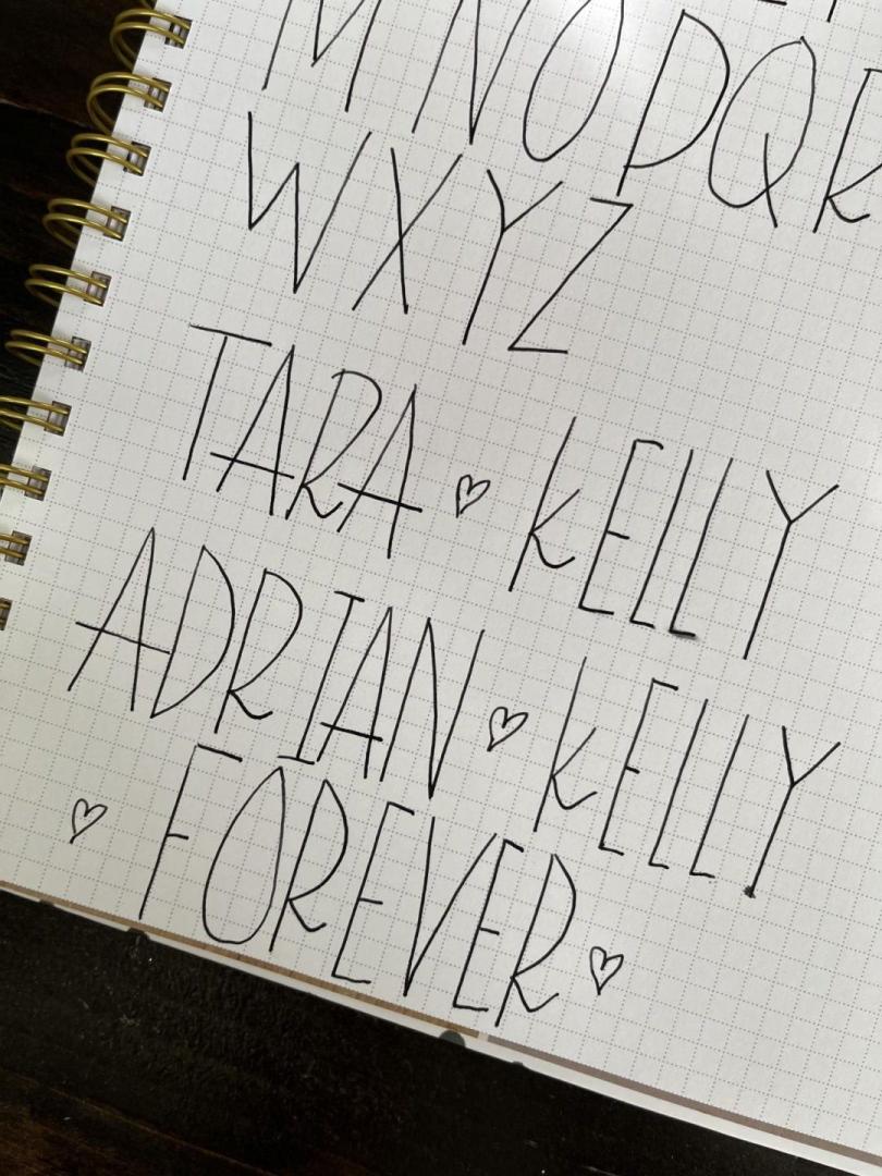 A paper with hand lettered words is shown as part of calligraphy practice.