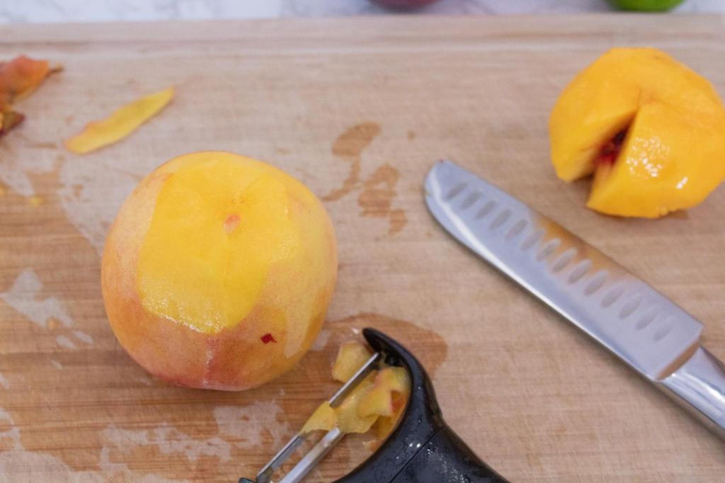 A peach is being peeled with a vegetable peeler.