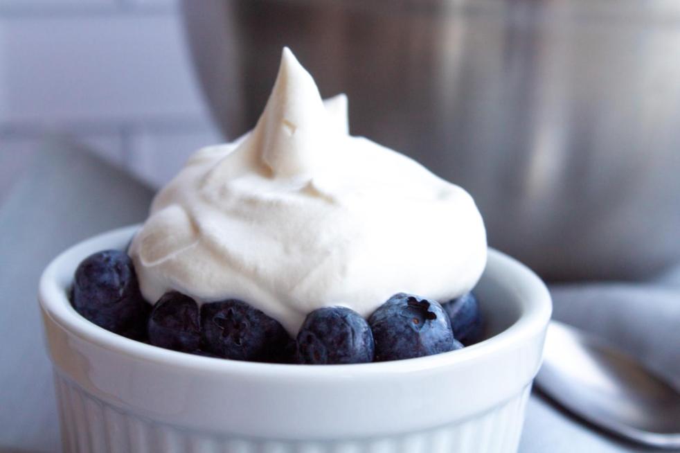 A woman shows a bowl of blueberries with fresh whipped cream after learning how to make whipped cream with heavy cream.
