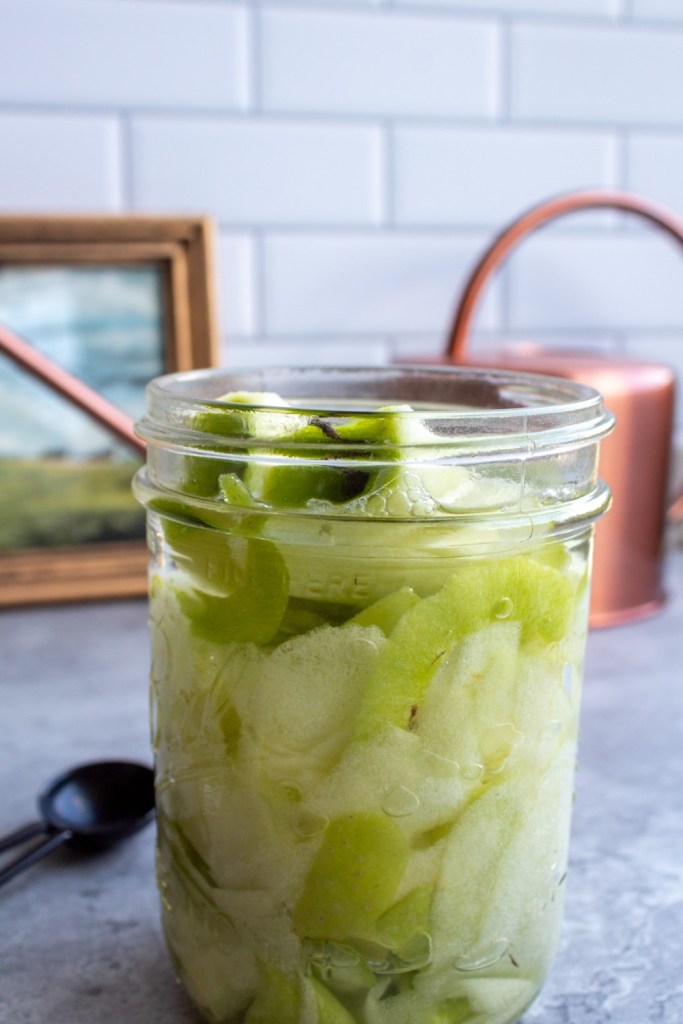 A woman stuffs apple scraps into a glass jar as she learns how to make apple cider vinegar with scraps.