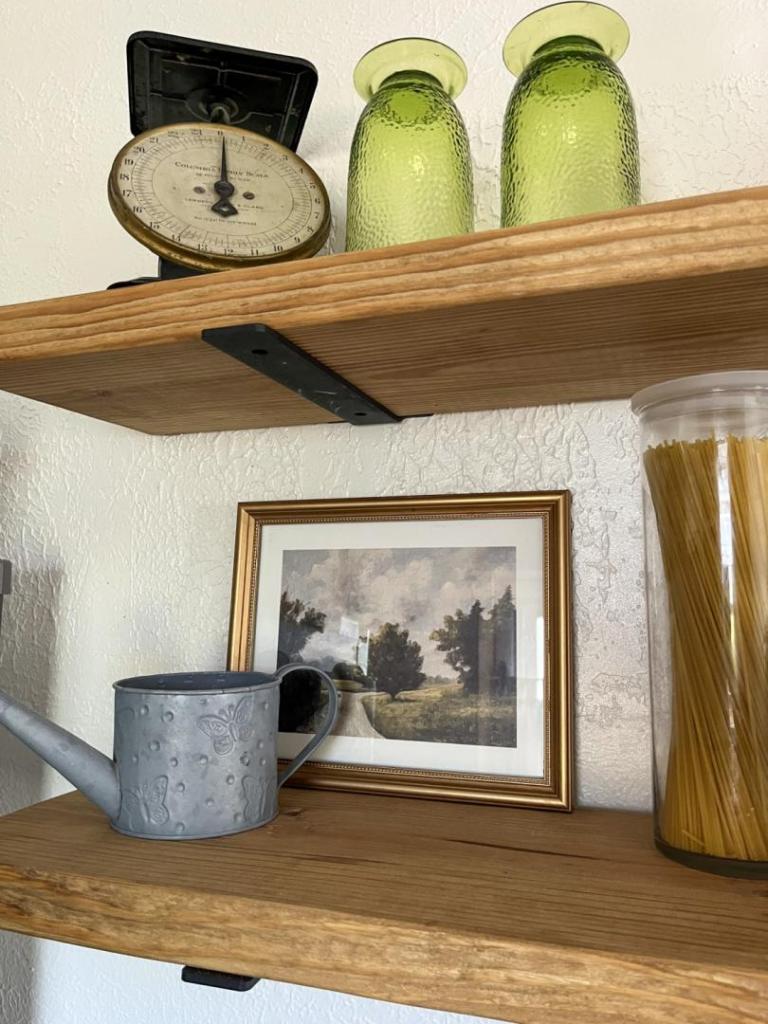 Art and a vintage scale are on display on open shelves in a kitchen.