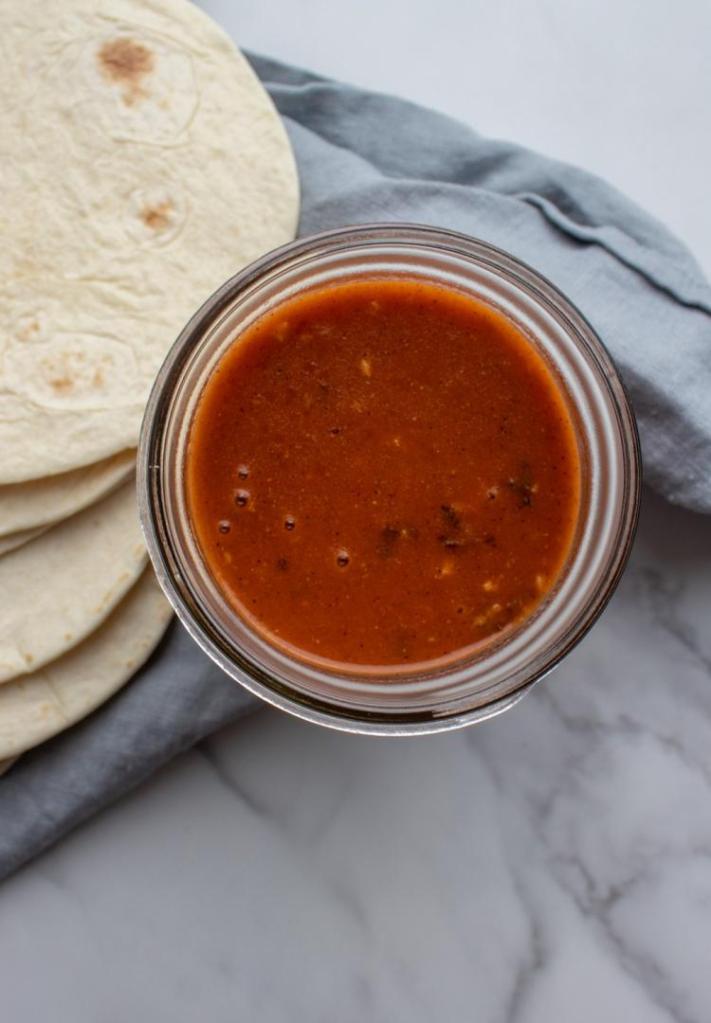 Easy red enchilada sauce is jarred alongside some tortillas.