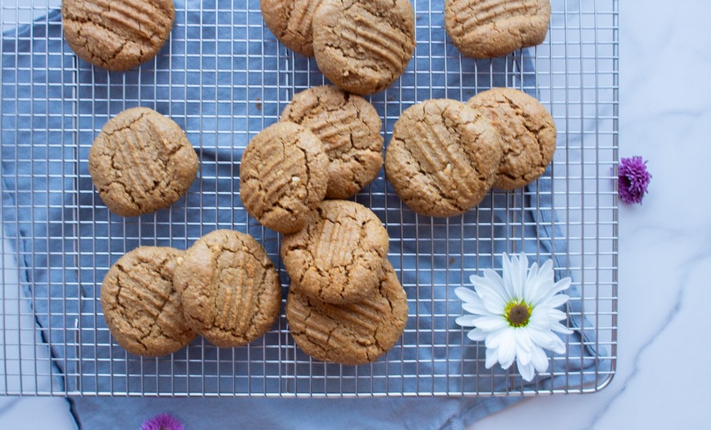 Thick, cake refined sugar free peanut butter cookies are cut in half and stacked on a cooling rack.