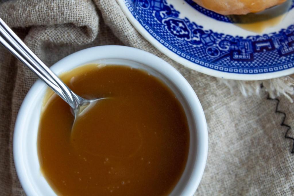 Smooth, creamy butterscotch sauce is in a white ramekin with a spoon in it.