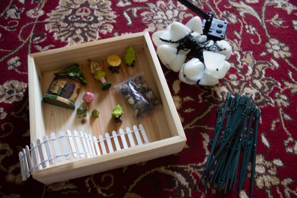 Lots of outdoor fairy garden supplies are laid out on a burgundy rug.