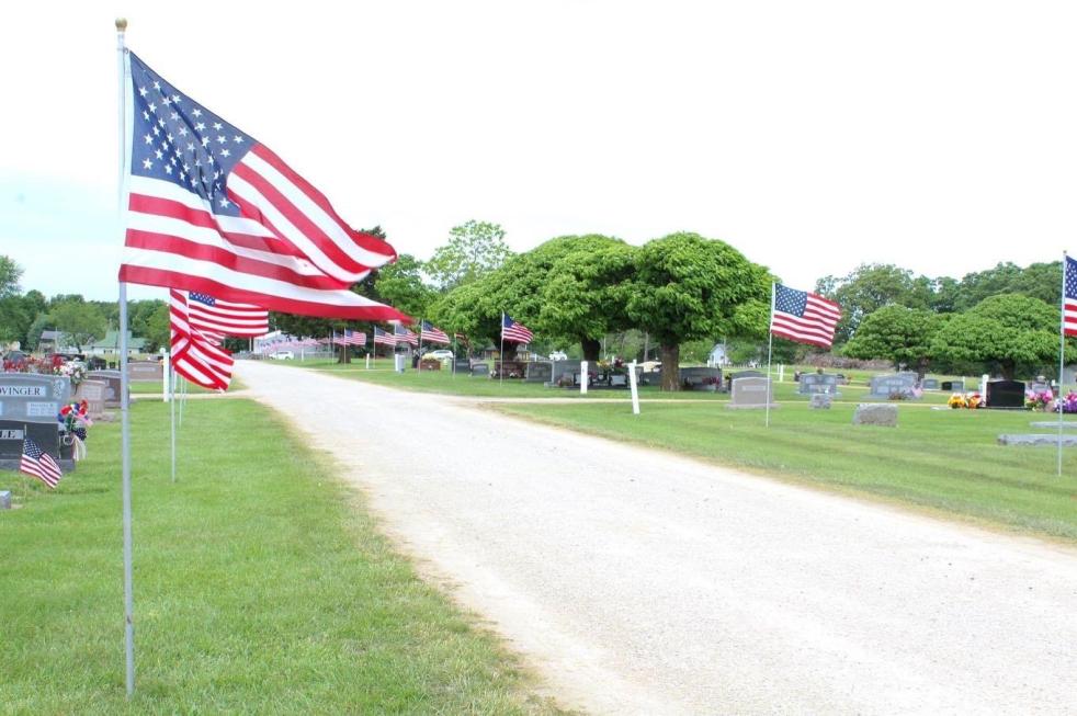 Fourth of July American flag is flying in the wind alongside other flags in a cemetery.