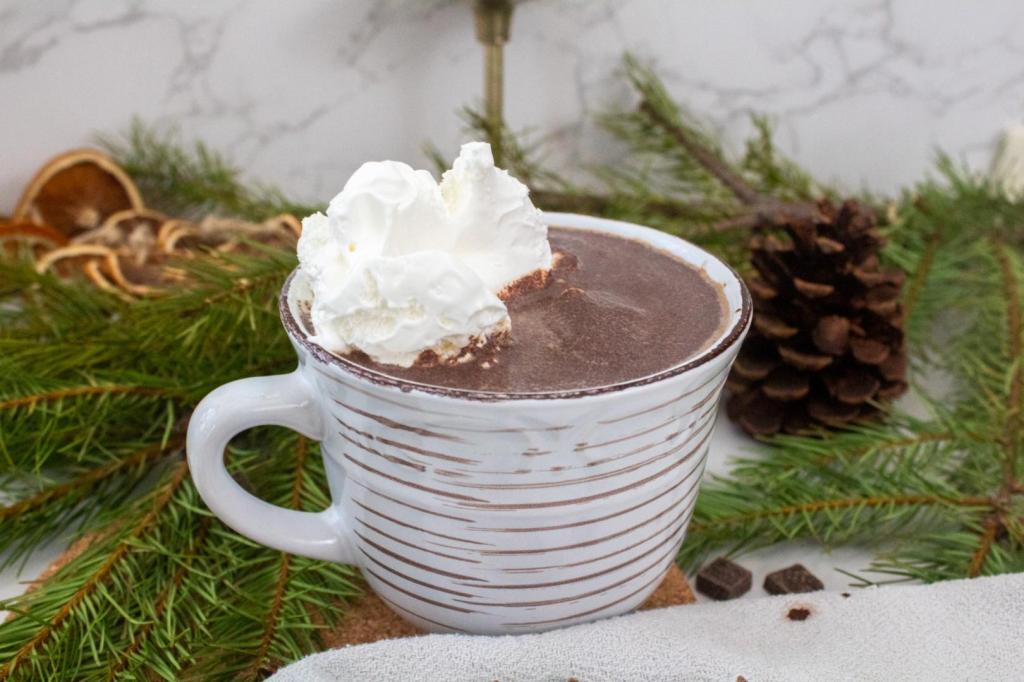 Refined sugar free hot chocolate is topped with whipped cream and is surrounded by evergreen branches and pine cones.