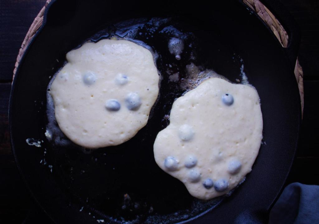 Pancakes cook in a hot cast iron skillet before flipping.