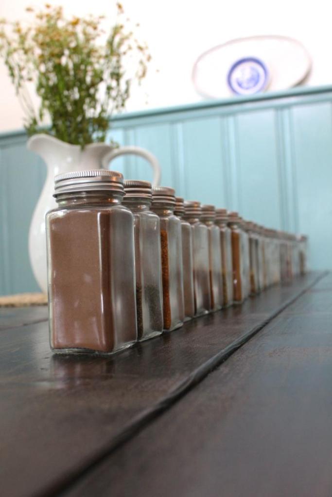 Spices and herbs are all lined up on a kitchen table.