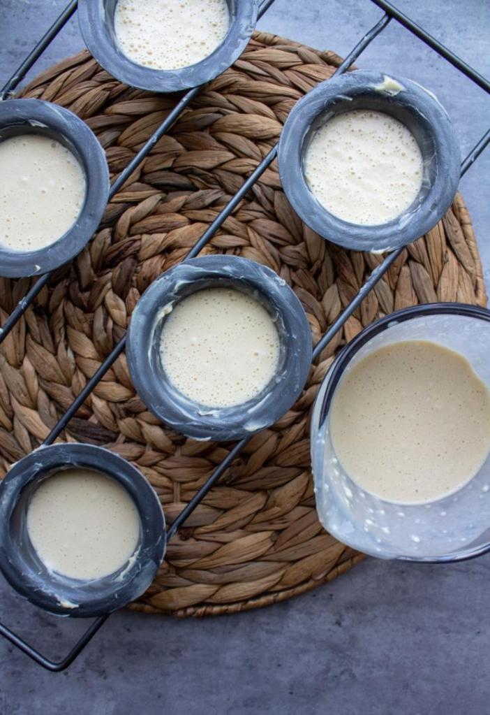 A batter is poured into popover tins using a liquid measuring cup.