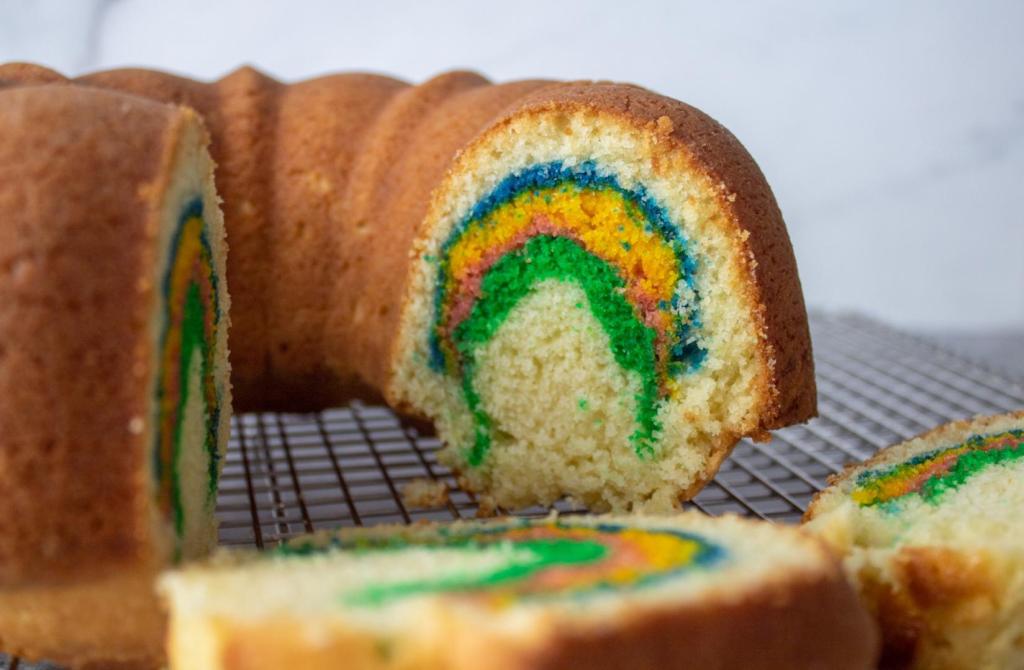 A rainbow bundt cake is sliced and ready to be served.