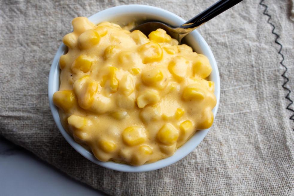 Cheesy creamed corn is served in a ramekin with a spoon on top of a tan linen.
