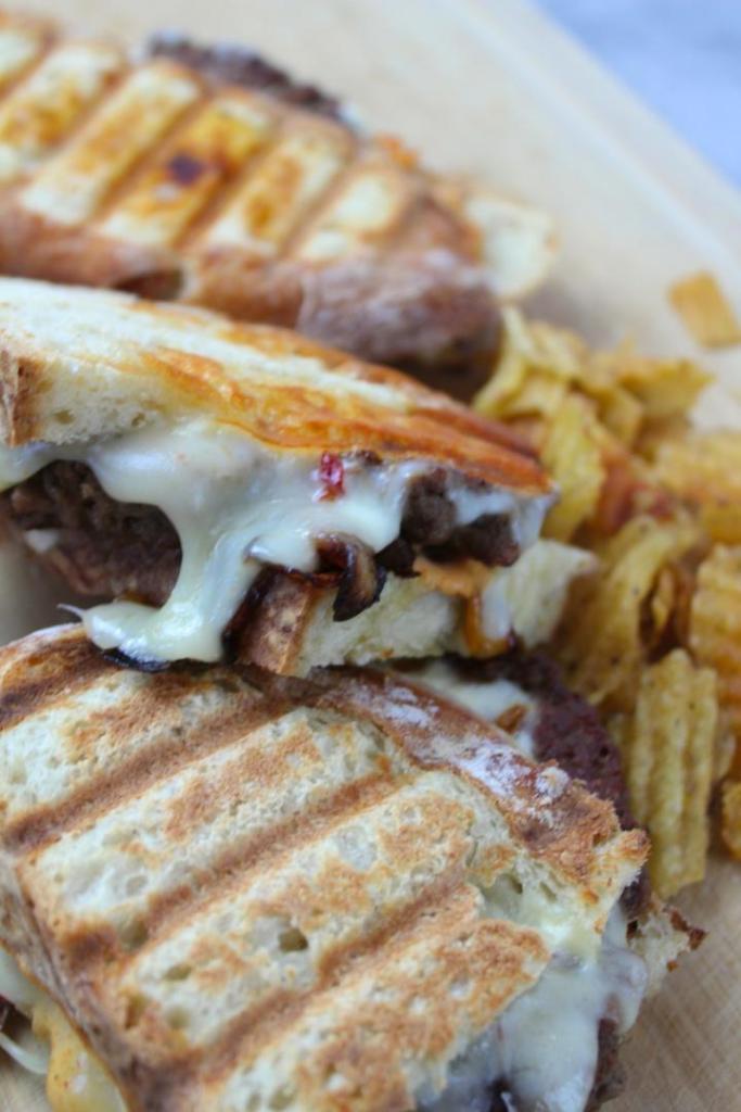 A delicious patty melt recipe has been stacked one on top of the other alongside some potato chips.