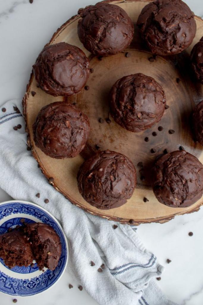 Double chocolate zucchini muffins are served on a platter with chocolate chips scattered around it.