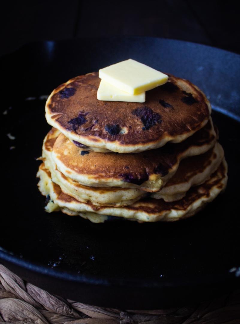 Extra fluffy blueberry buttermilk pancakes are stacked in a cast iron skillet before serving.