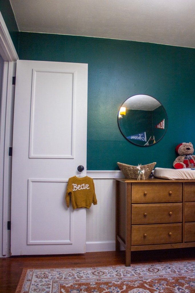 A chestnut colored dresser is shown with a black mirror and hanging sweater on a doorknob near the entryway.