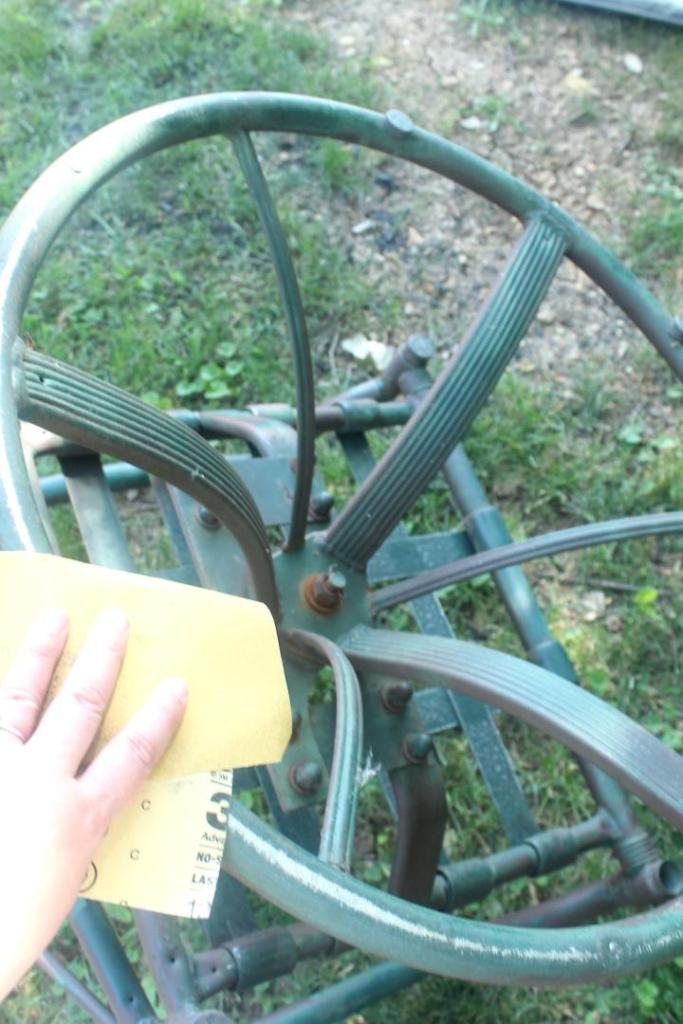 A woman is sanding a metal patio chair in her yard.