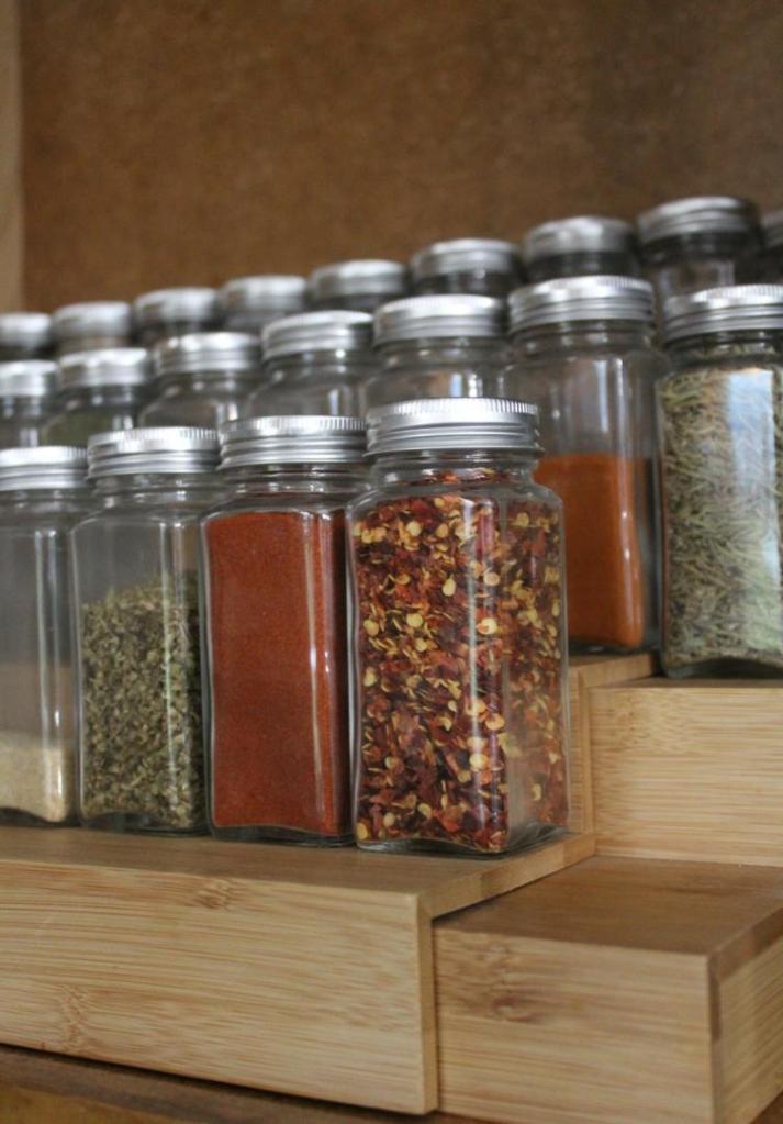 Brightly-colored spices sit on a tiered bamboo spice rack after being organized.