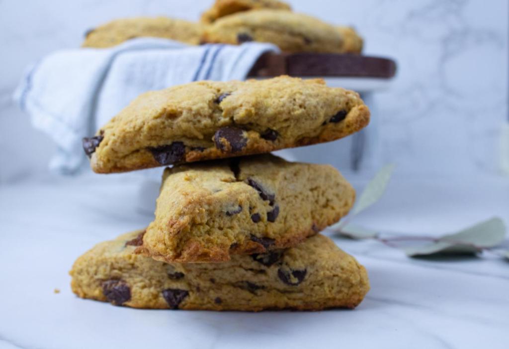 Pumpkin chocolate chip scones are piled high in front of a cake platter of more scones.