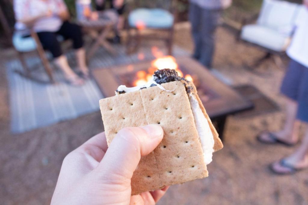 S'mores are being held up in front of a lit fire on a patio during an adult game night.