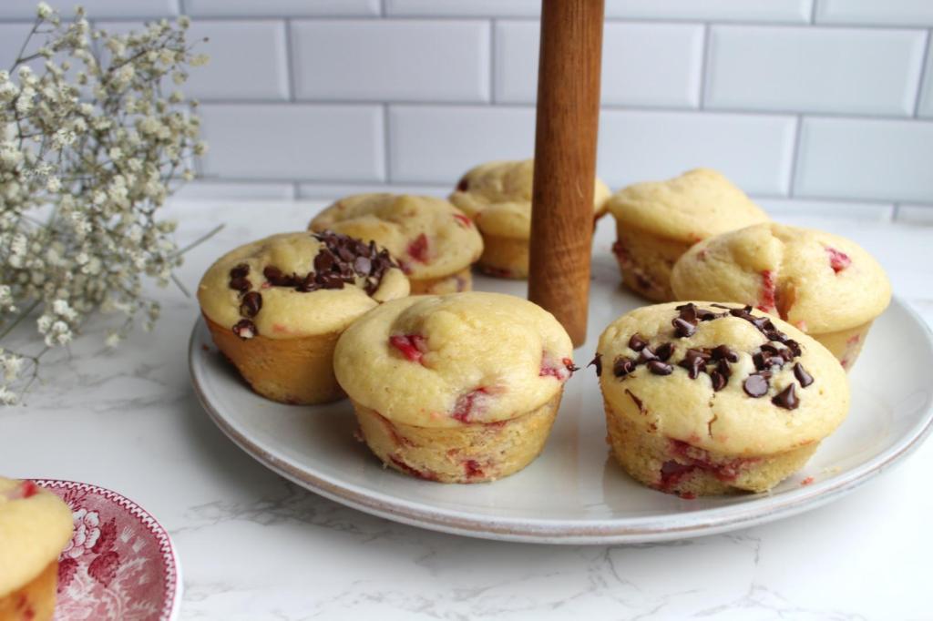 Strawberry muffins, some with chocolate chips, are arranged on a serving tray next to flowers.