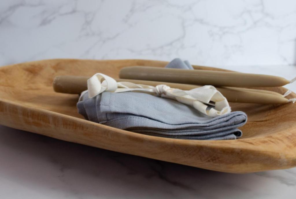 A wooden bowl has candles and napkins lying in it after a woman learns how to bleach wood decor with Clorox.