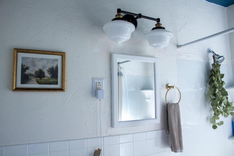 An updated cottage bathroom has gold hardware, a Miss Mustard Seed landscape art print, and a vintage-style art fixture.