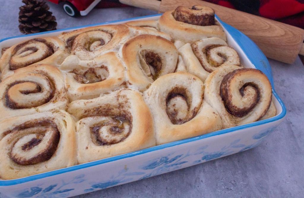 Cinnamon rolls are finished baking and sit on a kitchen table next to a rolling pin.