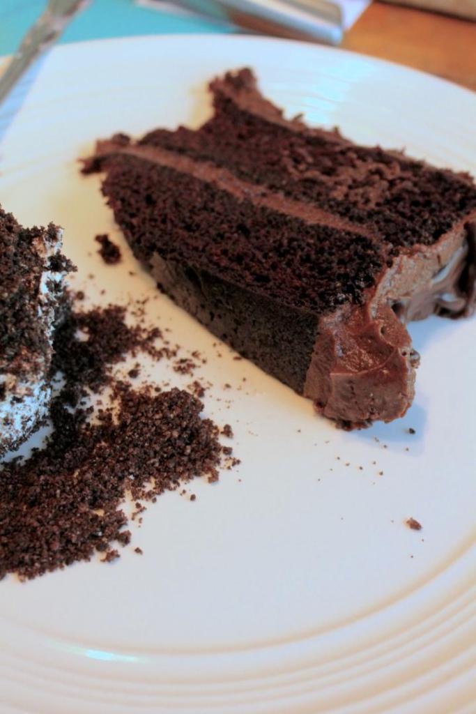 A rich chocolate cake slice sits on a plate alongside a piece of Oreo dirt cake.