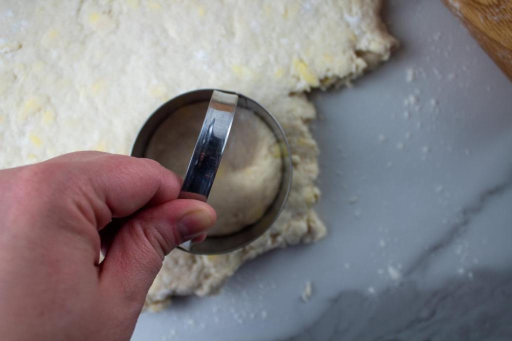 A woman uses a biscuit cutter to make disks of dough.
