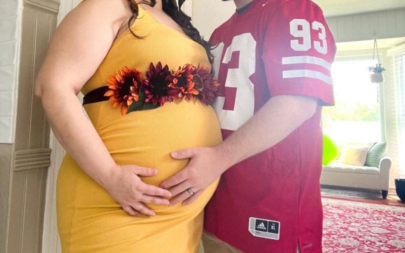 A woman wears a DIY sash belt for her baby shower as her husband embraces her.