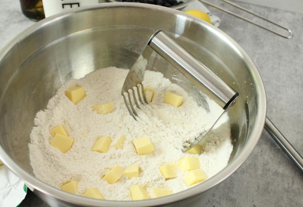 Using a pastry blender, a dough begins with cubes of butter added to flour.