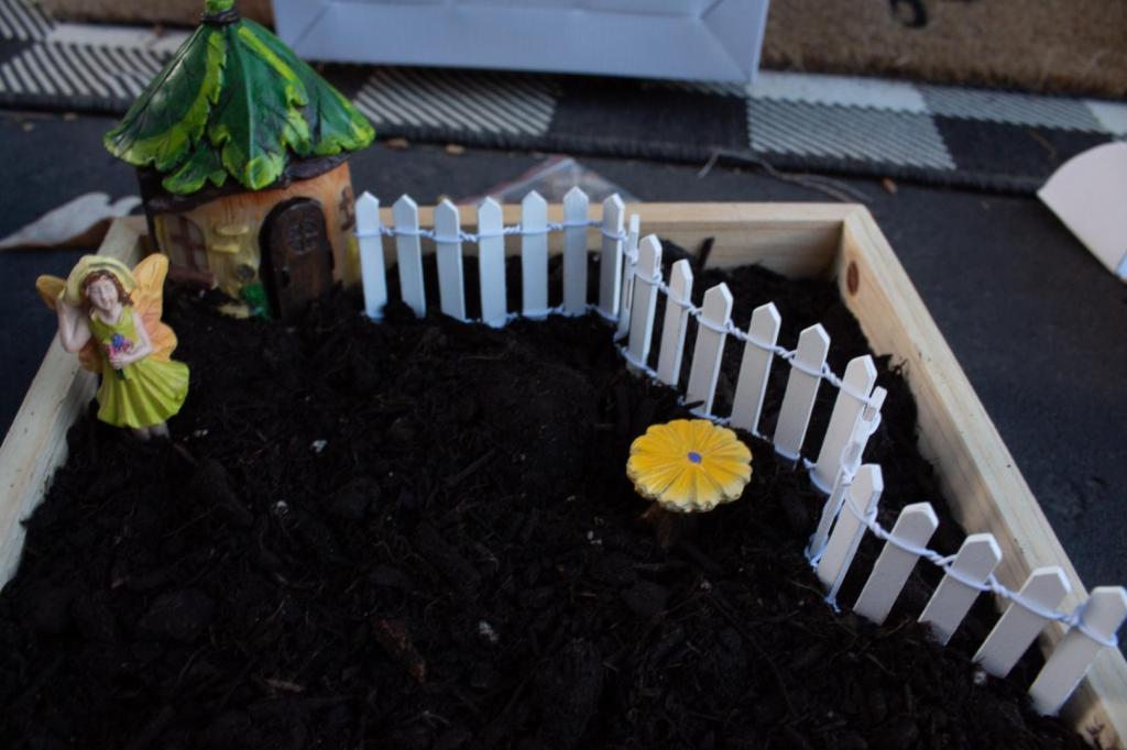 A fairy is added to her garden along with a cottage and picket fence.