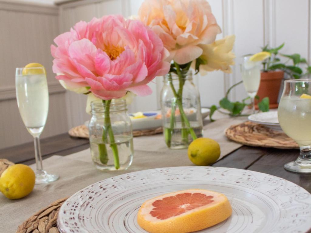 Large flowers are placed in glass jars in the center of a summer table setting.