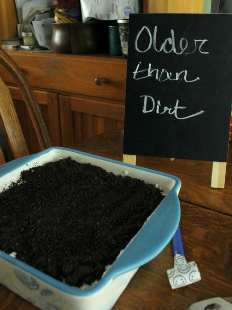 A dirt cake has a sign next to it that reads "Older than dirt."