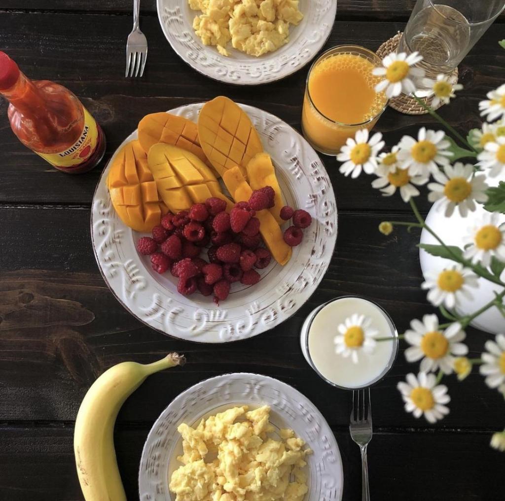 Flowers are near a breakfast spread on a table.