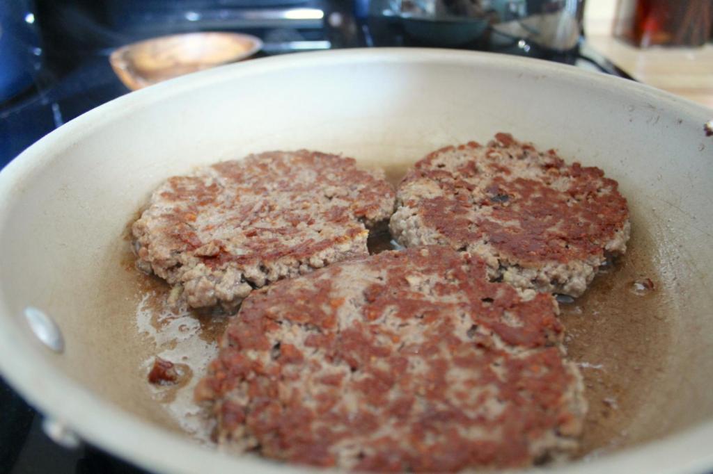 Three Impossible burger patties cook in a skillet.