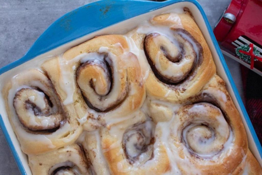 Classic, fluffy cinnamon rolls are in a casserole dish cooling on a dining table.
