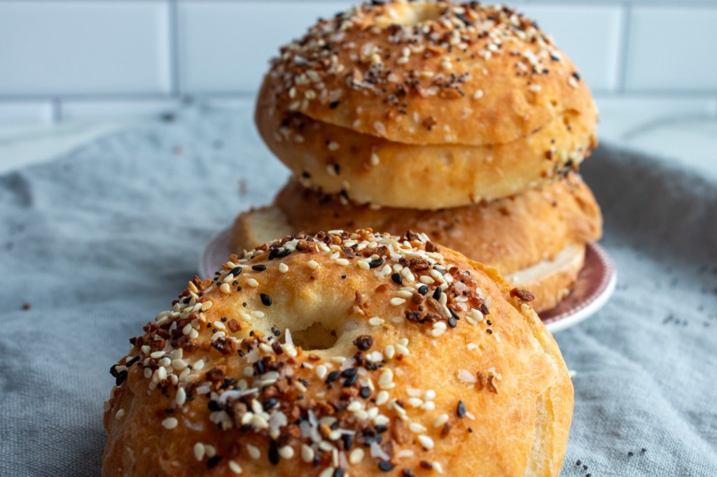 This easy bagel recipe with yogurt depicts three everything bagels stacked on one another on a linen.